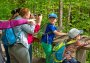 Group of visitors with children on the viewing platform: woman looking through binoculars, child standing at the railing, guide is showing something