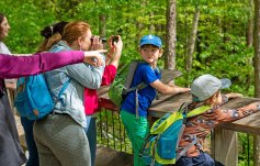 Besuchergruppe mit Kindern auf Aussichtsplattform: Frau schaut durch Fernglas, Kind steht am Geländer, Guide zeigt etwas